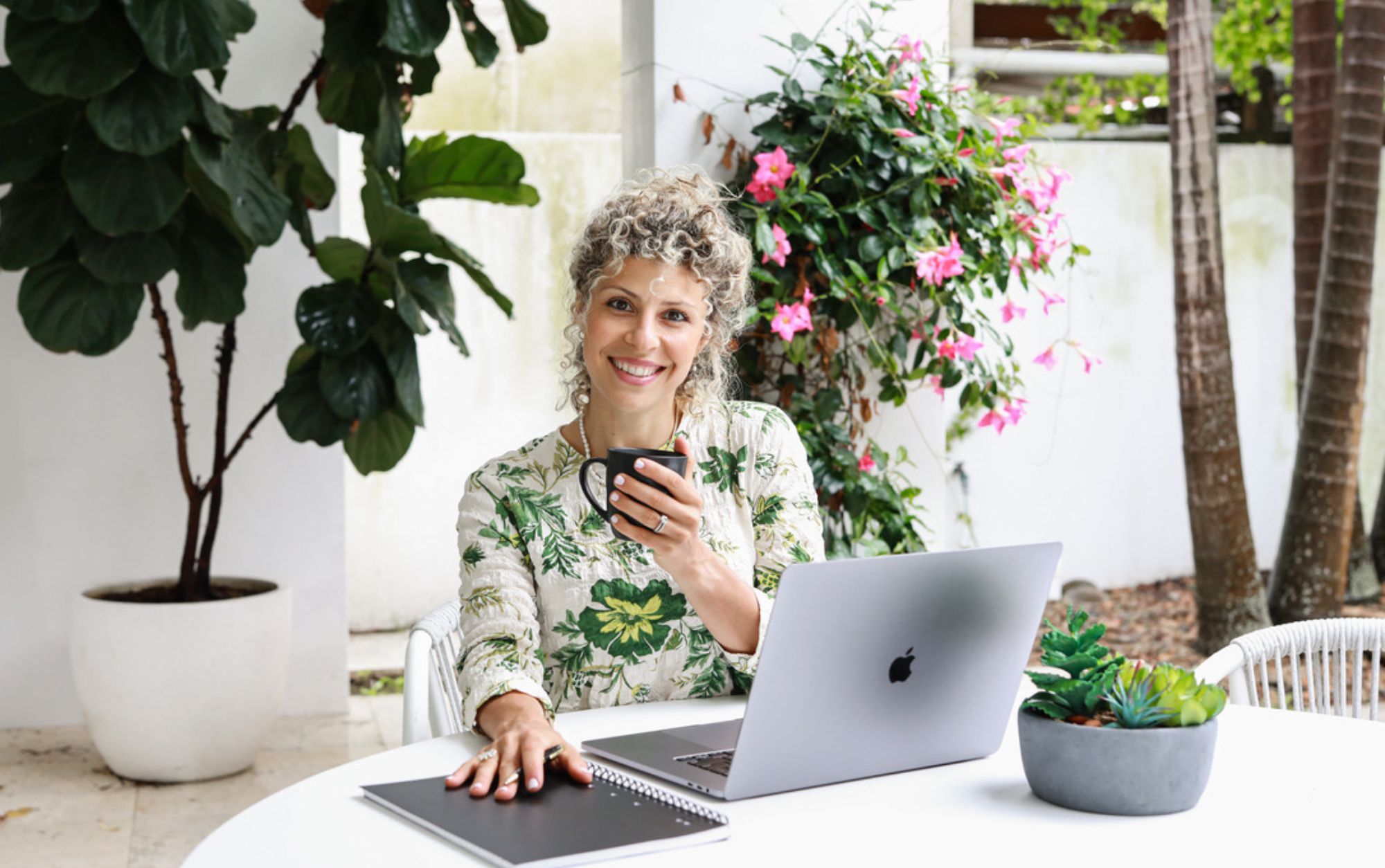 Women sitting at computer with coffee and nice pink and green flowers in background