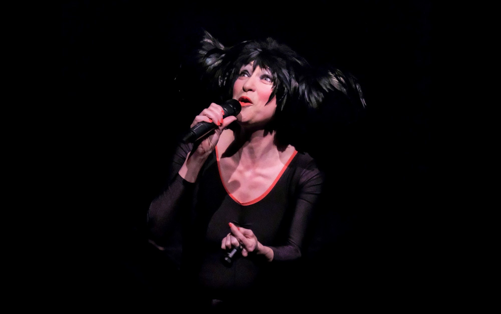 Image of woman with feathered hat and mircrophone singing on stage