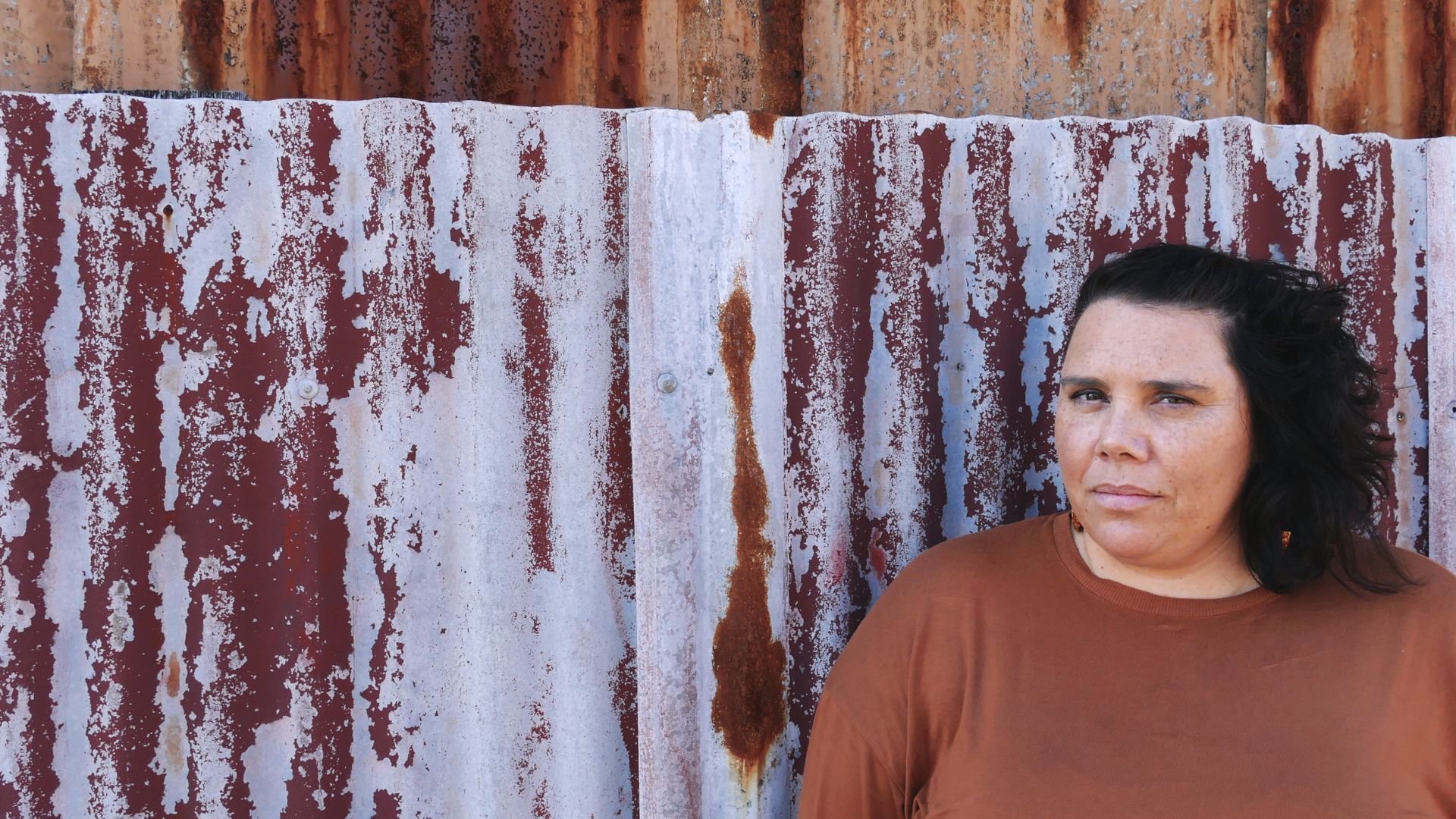 Author Nardi Simpson looks to the camera in front of a rusted iron fence