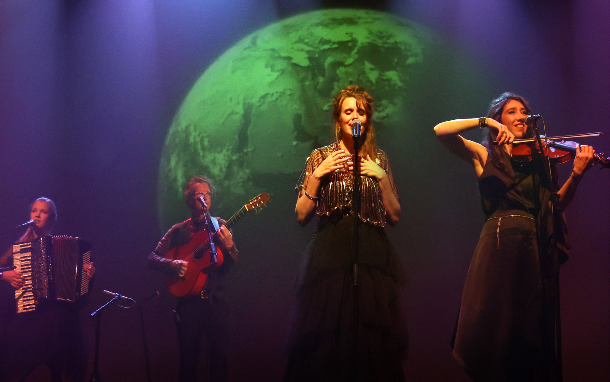 Four musicians on stage, with a video image behind them of a large green planet