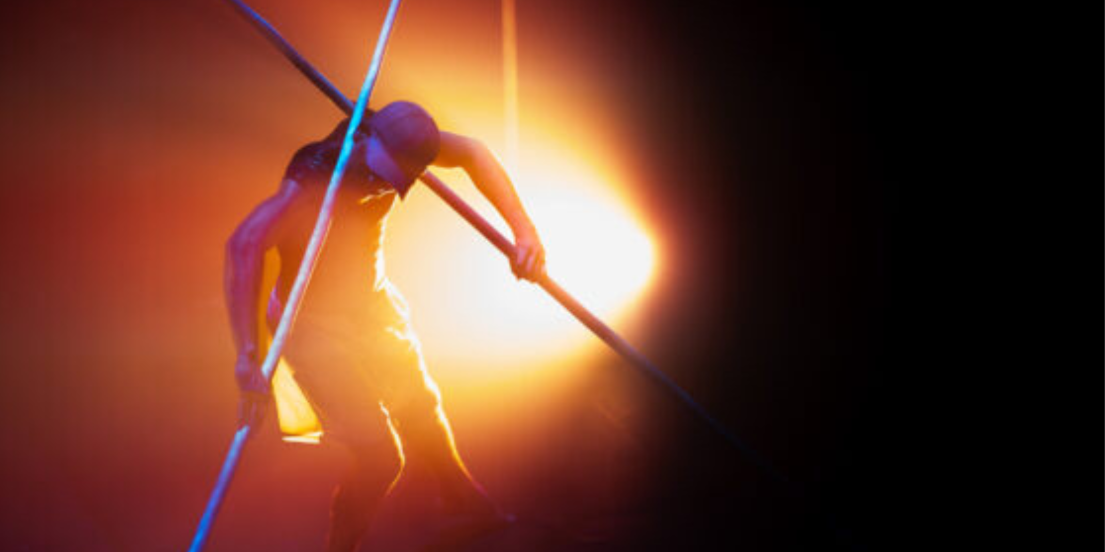 Image of a performer hanging over a acrobatic rail. Night time with yellow stage lights