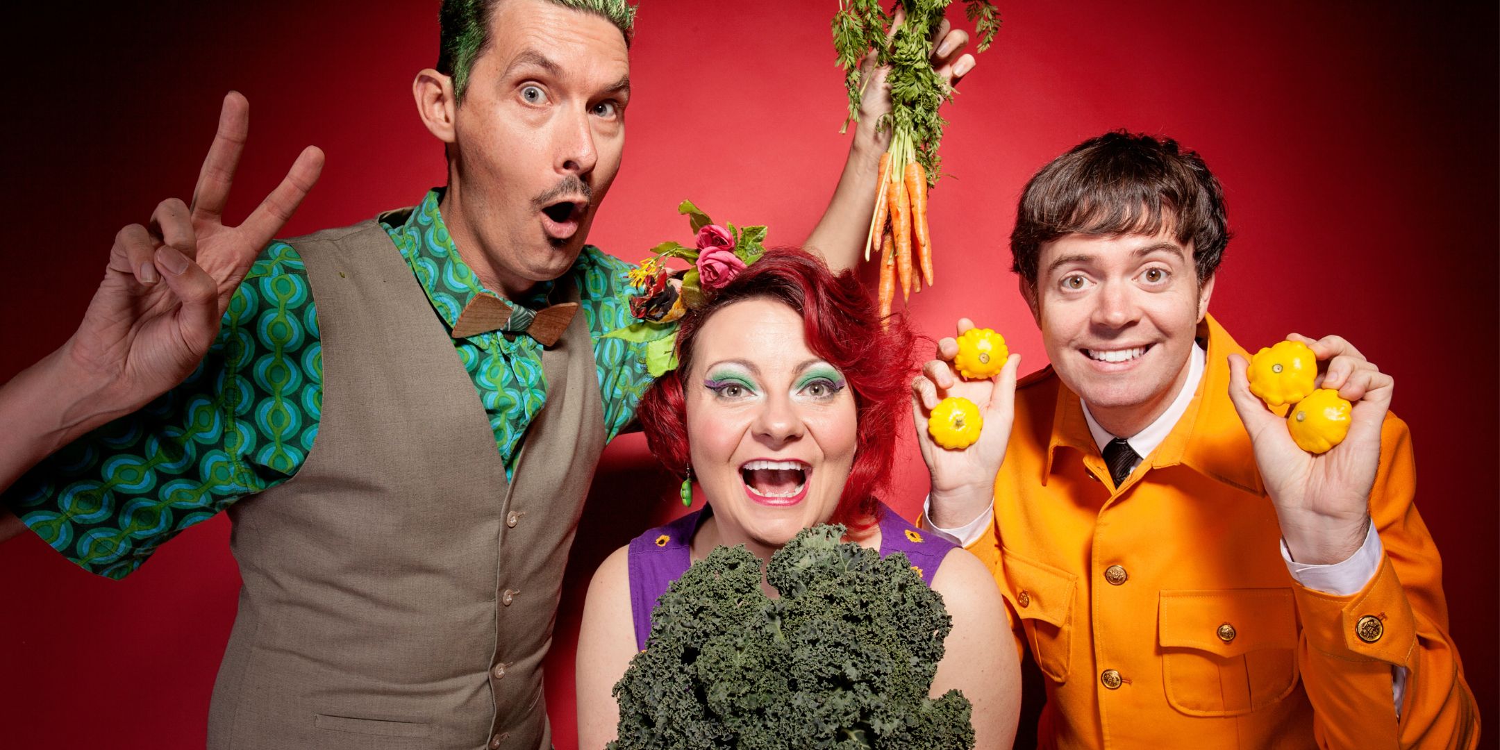 3 colourful characters facing the camera holding up carrots and broccoli and other vegetables