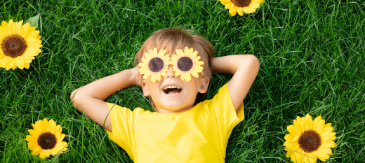 a child laying on grass with sunflower sunglasses in a yellow tshirt