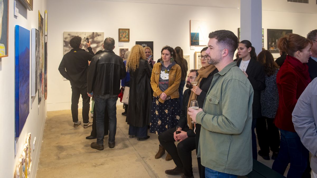 An photograph of a crowded Bondi Pavilion Art Gallery with many people having a good time within the space. Many artworks are around them. 