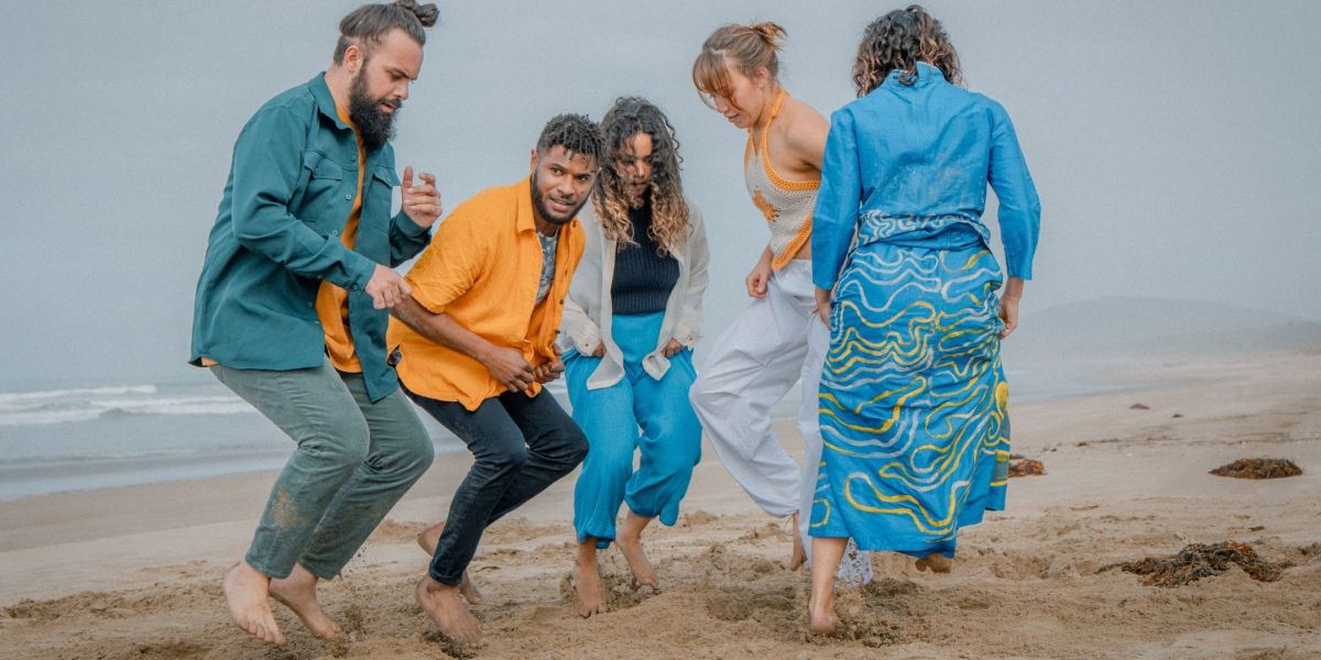 A group of dancers on a beach dancing in a circle