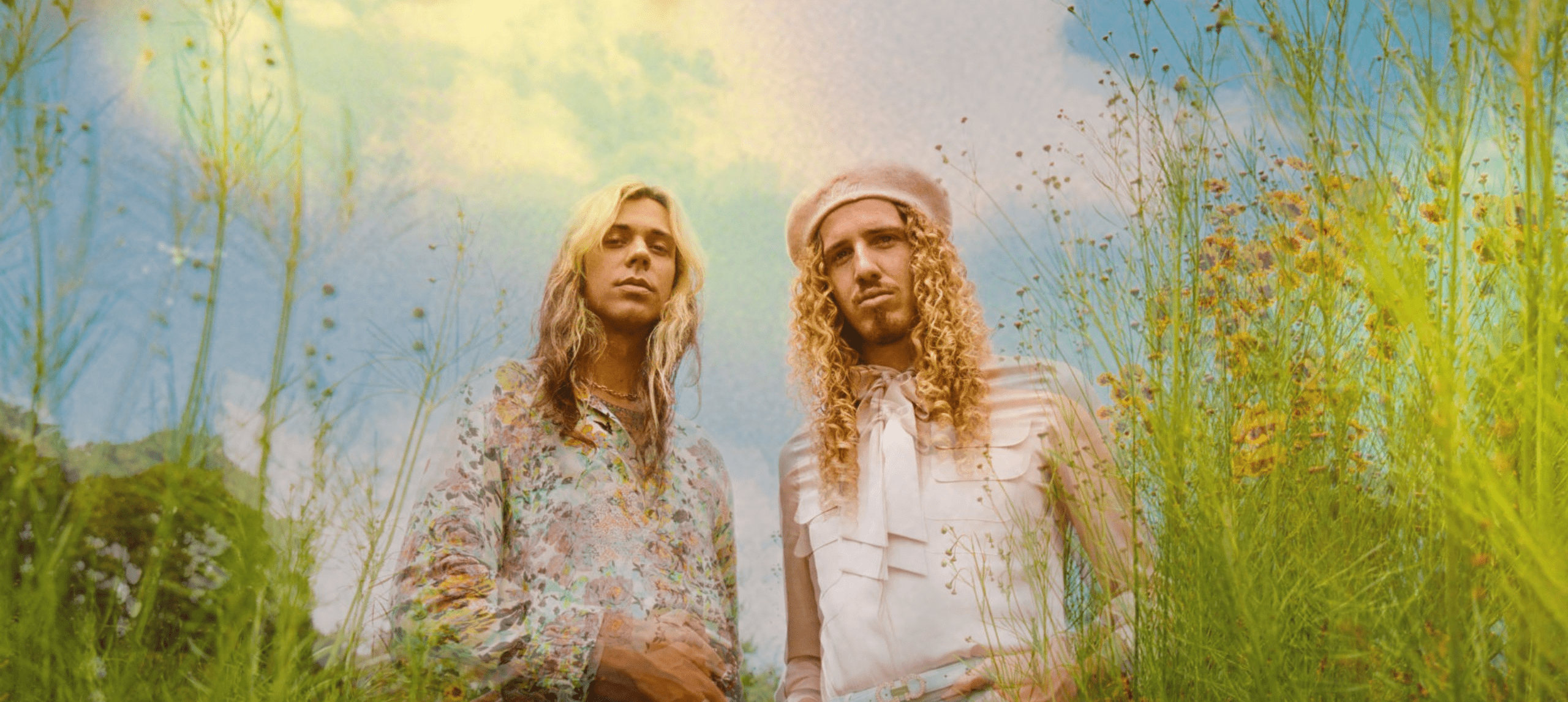 Two dreamy long haired musicians standing in long grass