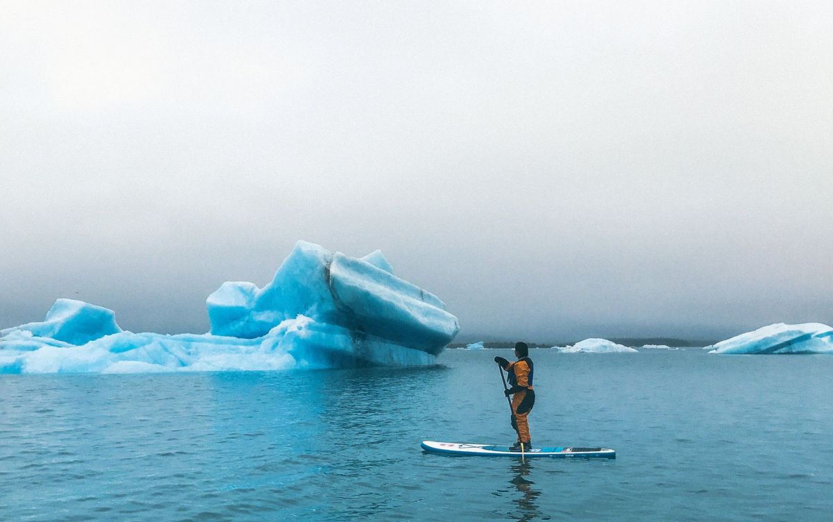 Stand up paddler in Alaska looking at massive ice berg