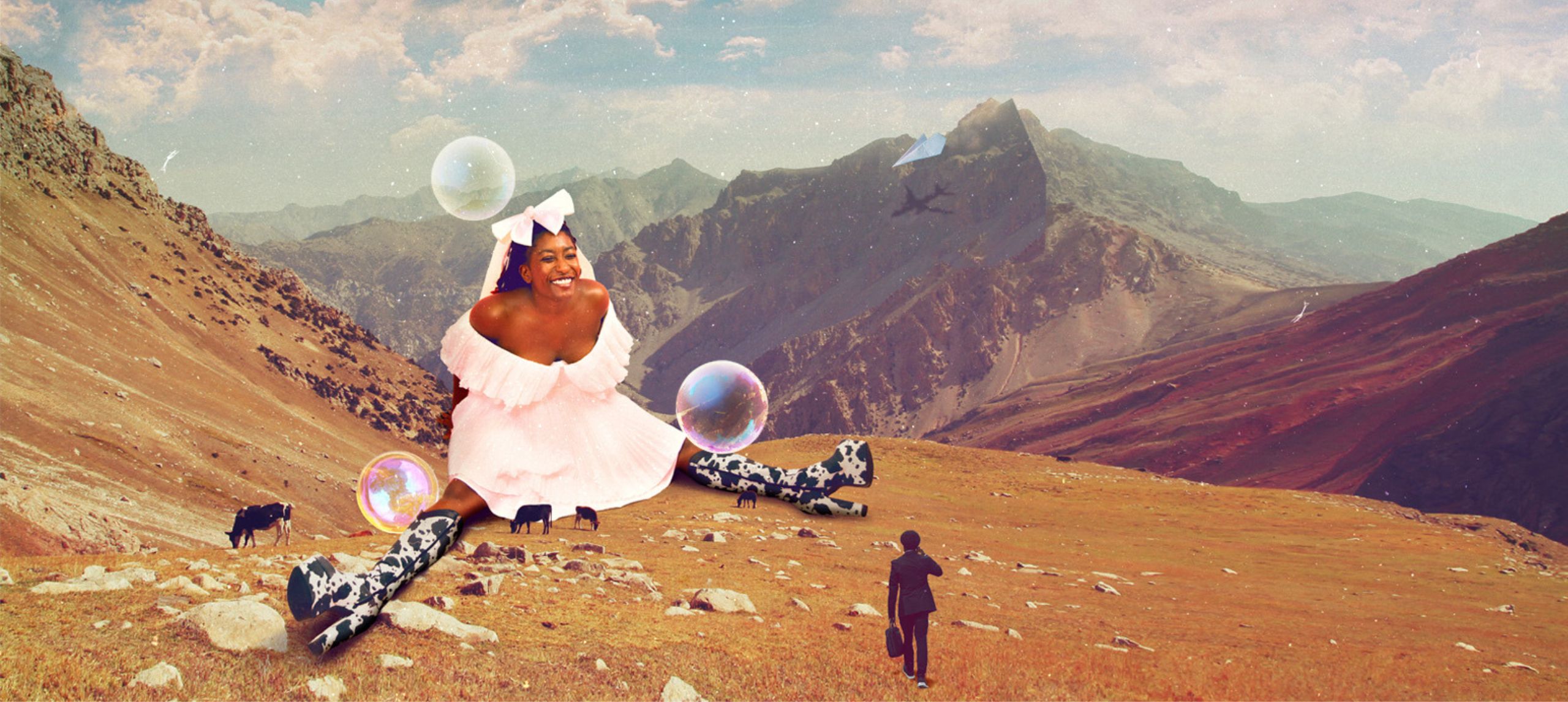 Sophie sitting in a valley with mountains in background dressed in frilly pink dress, laying on the ground with cowboy boots with cow print on them