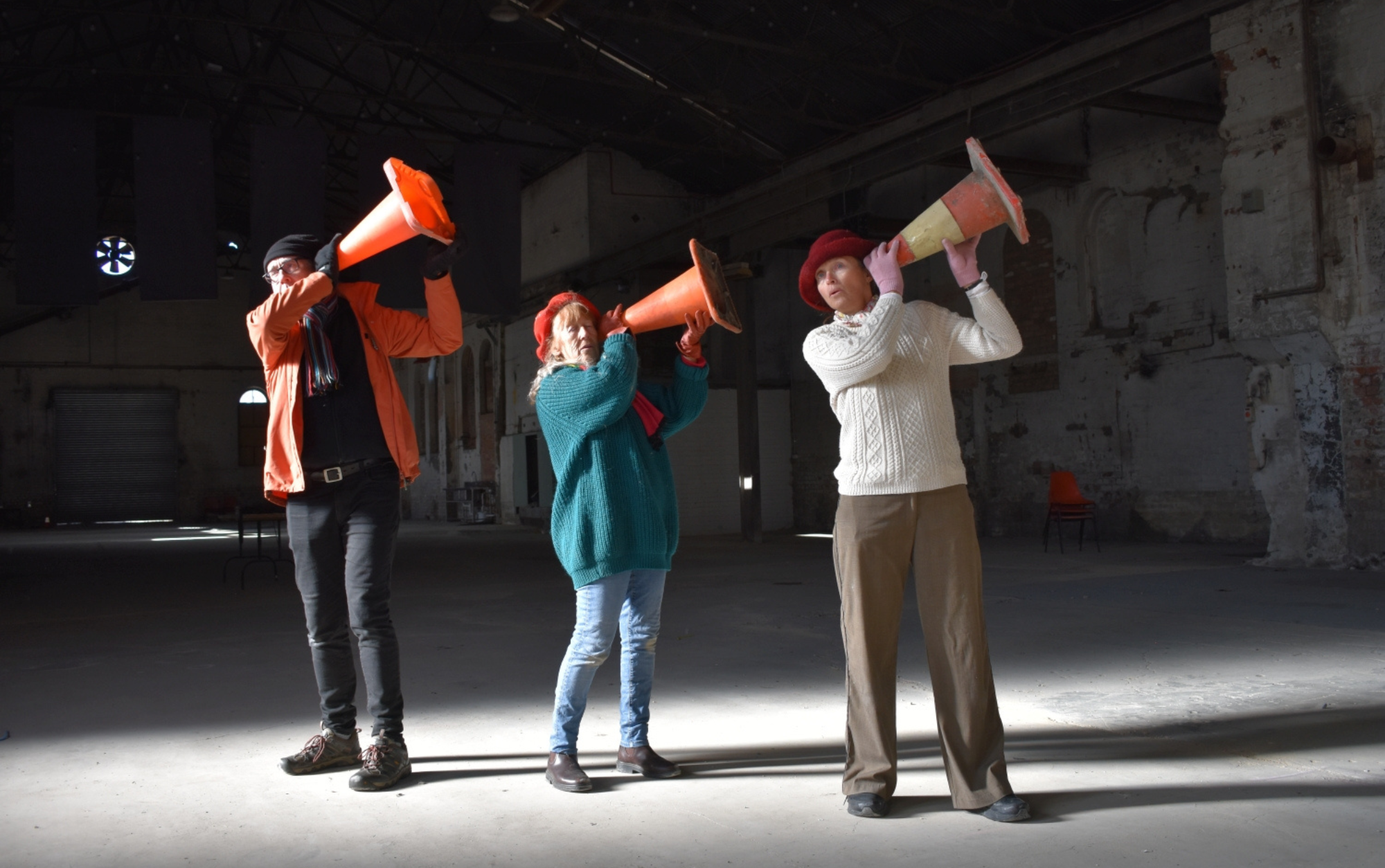 Three whacky vocalists in a warehouse with traffic cones up to their ears