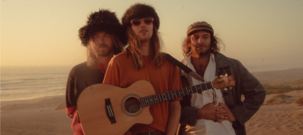 Three male musicians with a guitar on the beach