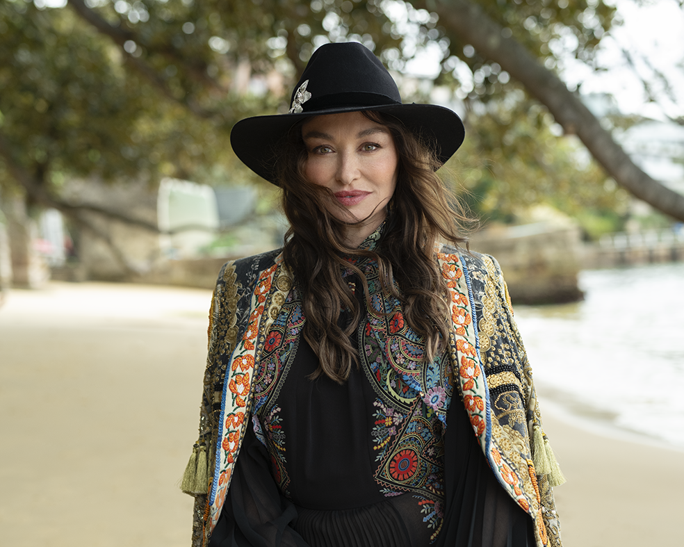 Woman with black hat and long brown hair stares at camera. 