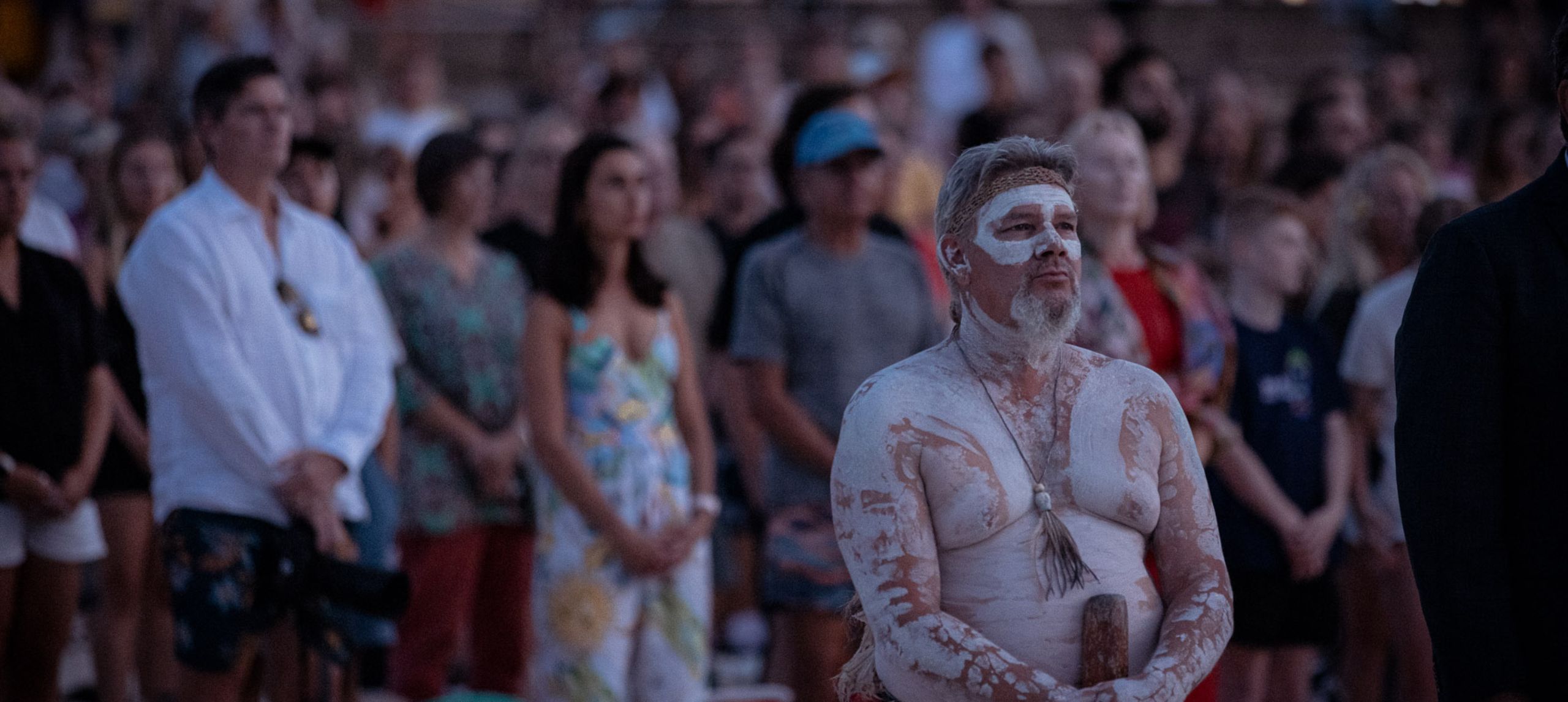 Image from the 2024 Dawn Reflection. First nations man stands on Bondi Beach with crowd standing behind him.