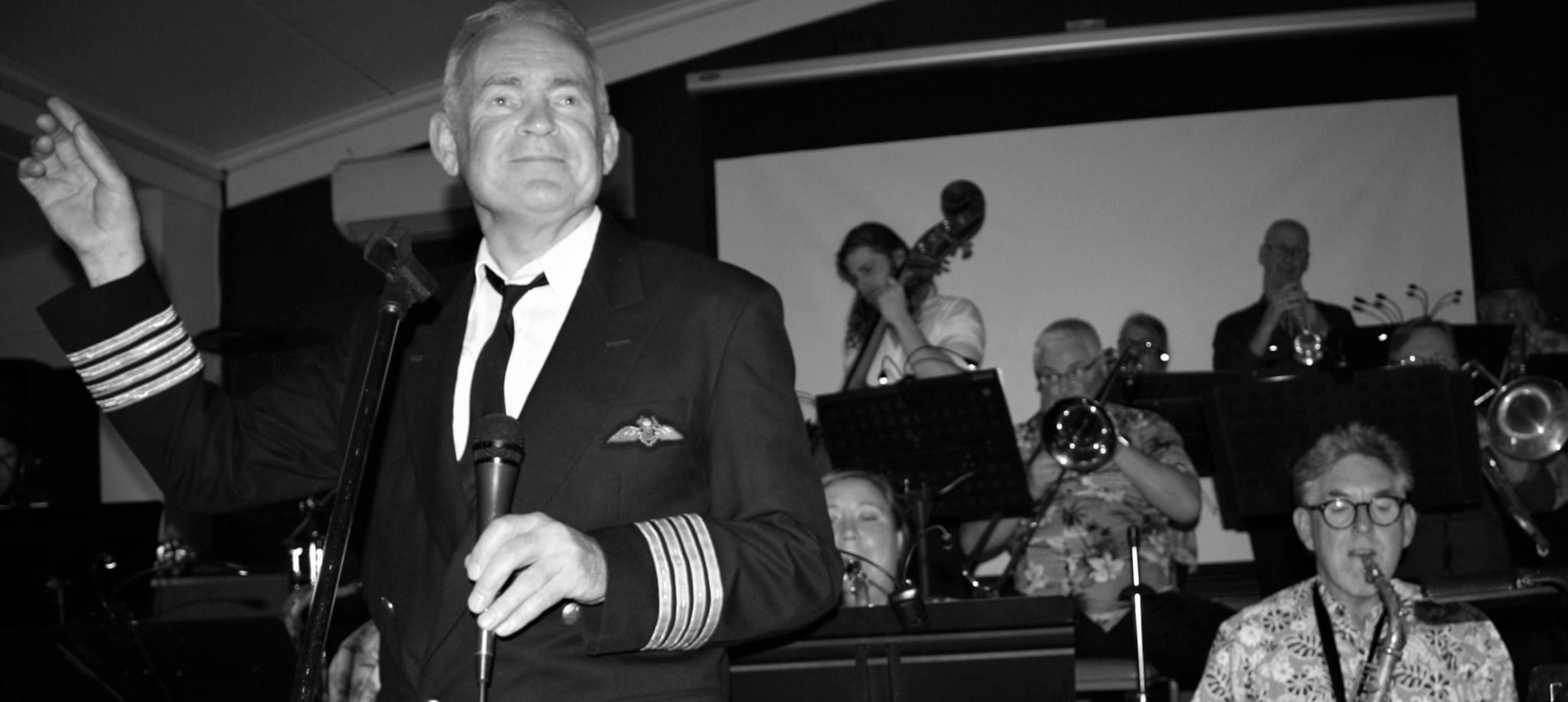 A jazz singer in a uniform in front of a big band B & W photo.