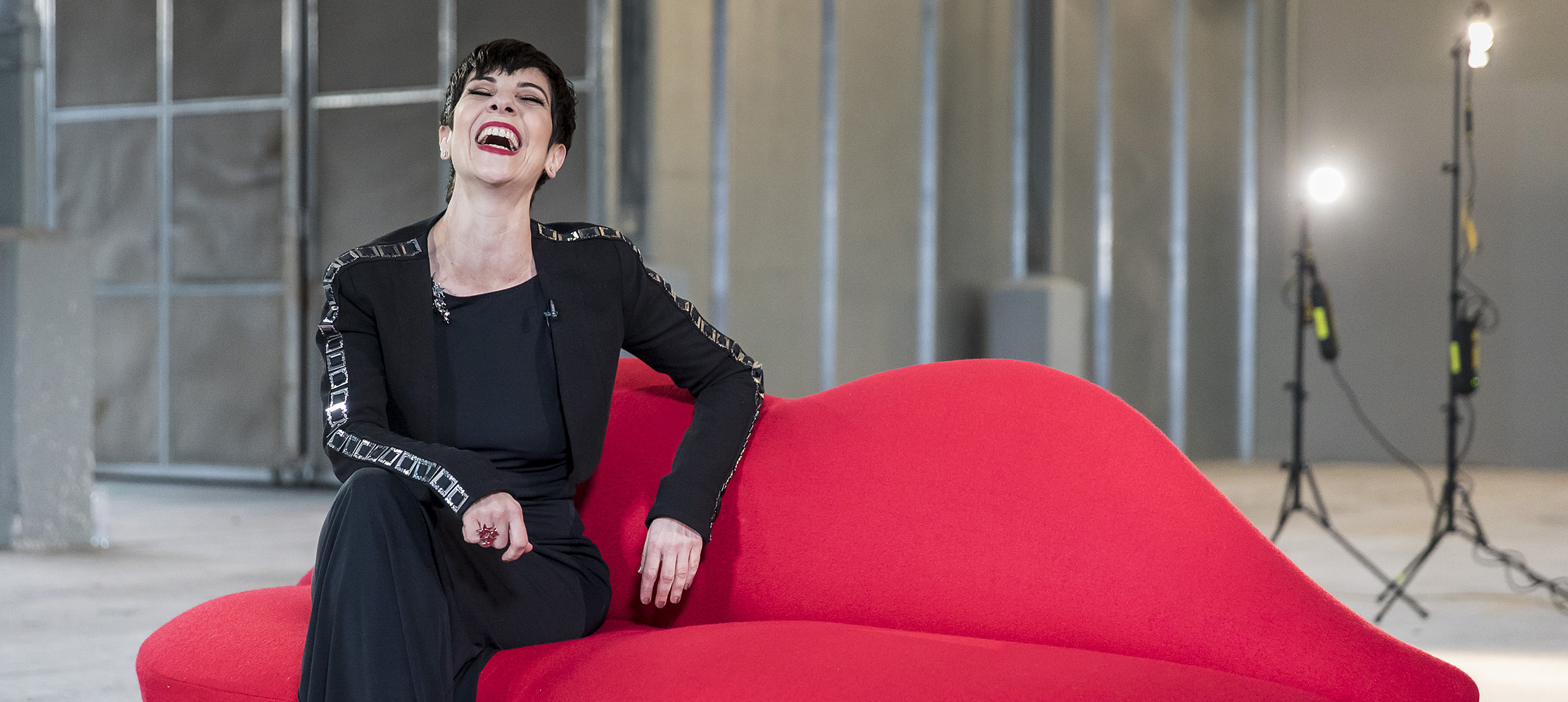 Phyllis Foundis sitting on a red lips couch laughing