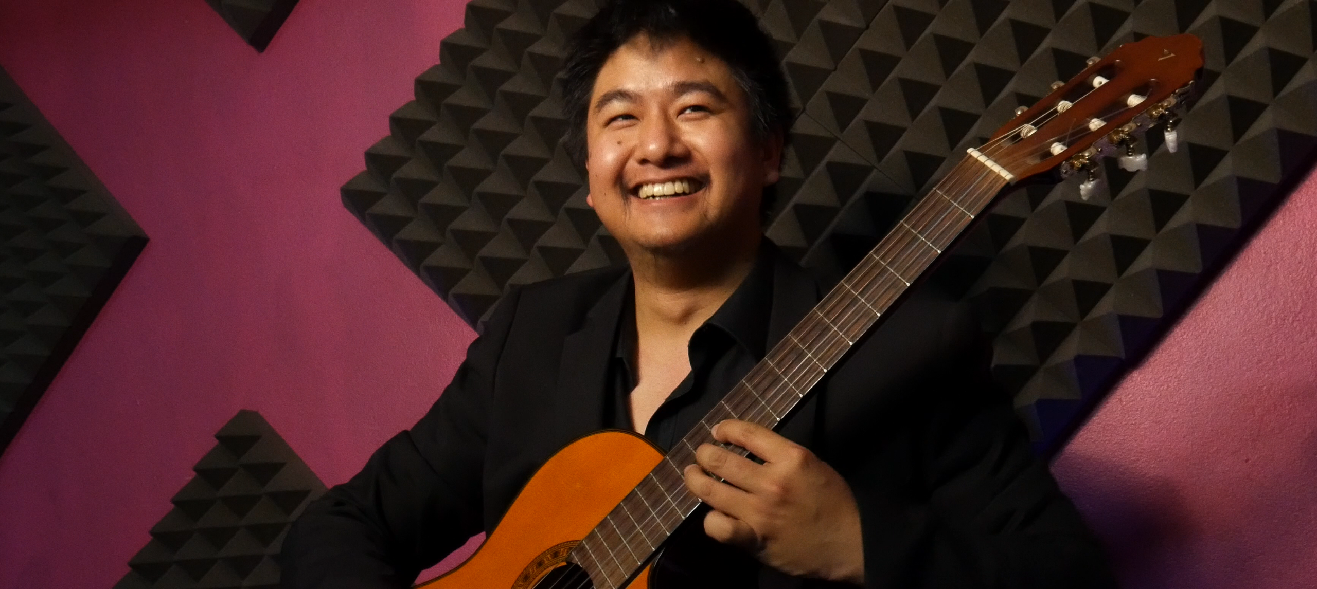 A smiling classical musician with guitar sitting down.