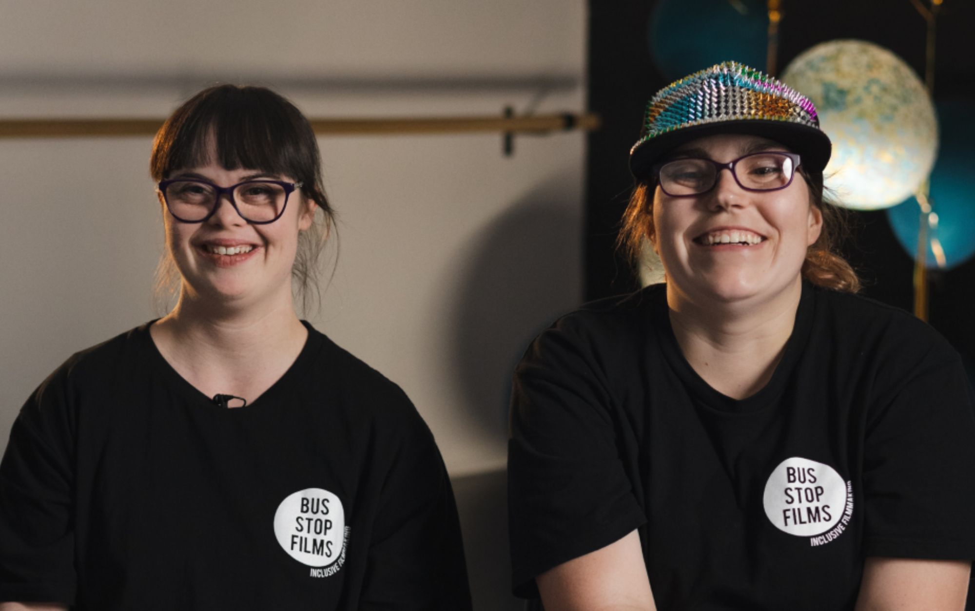 Two young women smiling with bus stop films t-shirts