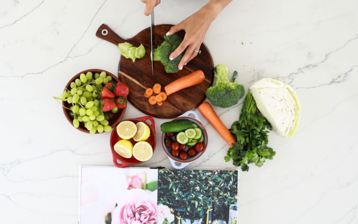 grapes, strawberries, lemons, carrots and brocoli on a table top with women chopping veggies