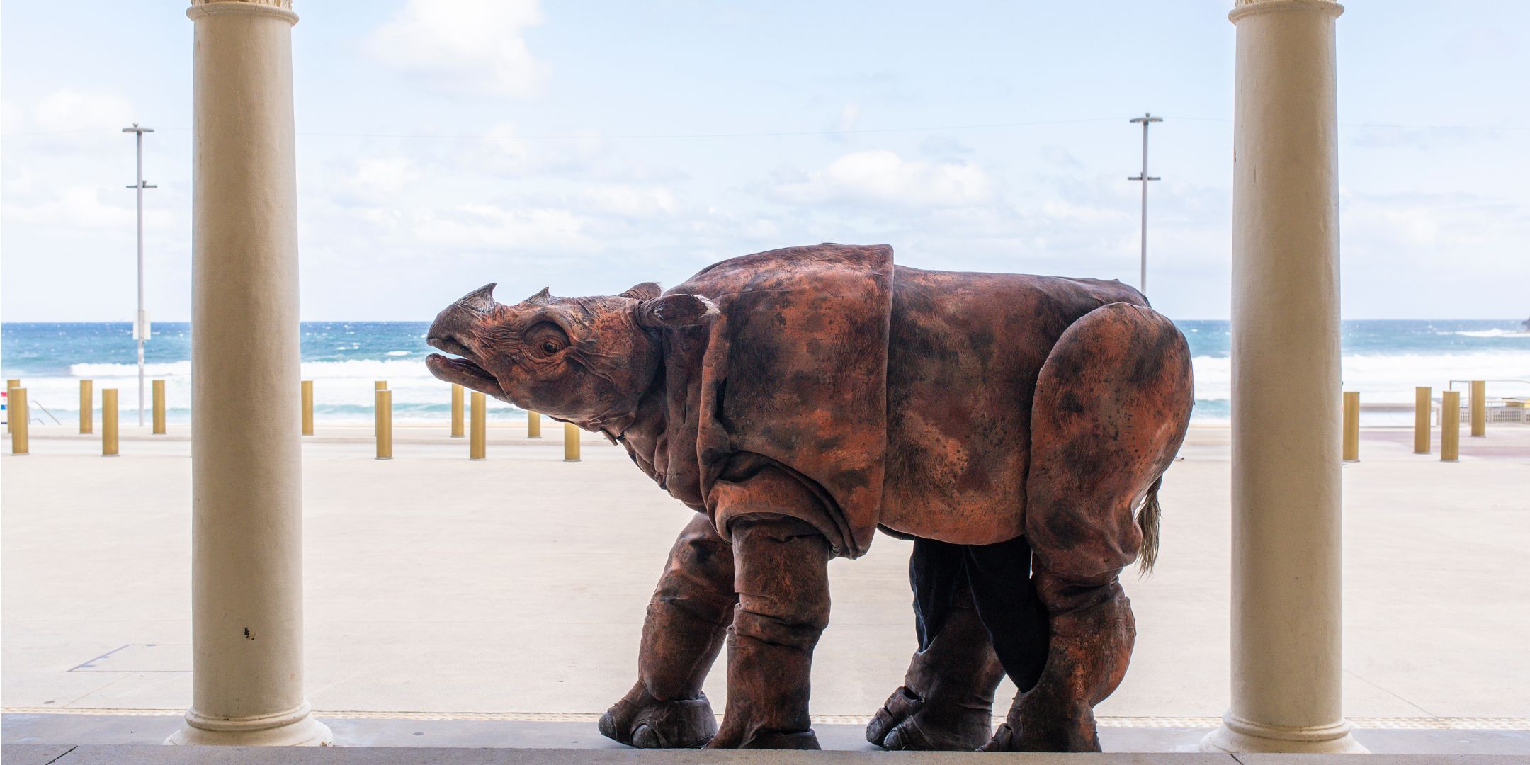 Giant Rhino puppet in Pavilion arches with the beach behind